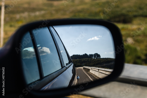 reflections in a mirror of a car driving by day   © luismicss
