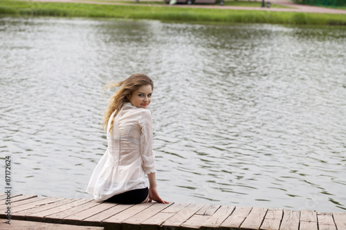 Young beautiful girl in a white tunic sits on a wooden pier on t © Andrey_Arkusha