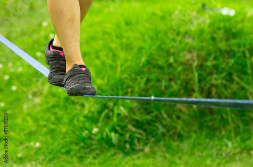 Closeup womans feet with shoes balancing on slackline and grassy background