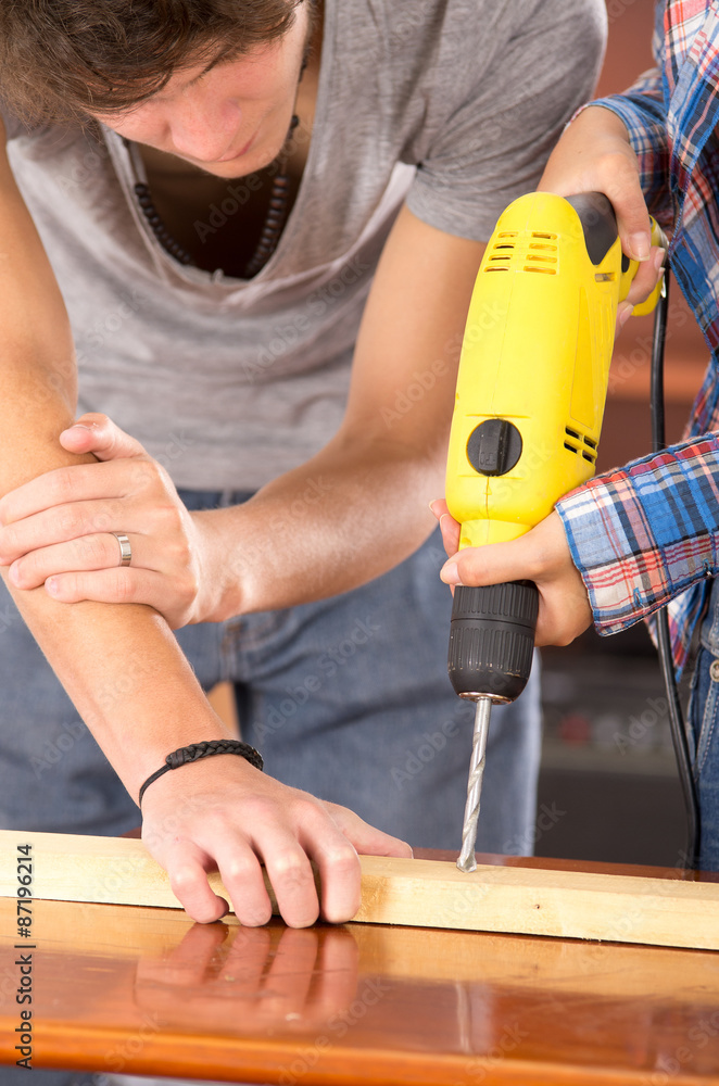 Closeup of couple working together as man holding wooden piece down on table while woman using power drill Closeup of couple working together as man holding wooden piece down on table while woman using power drill