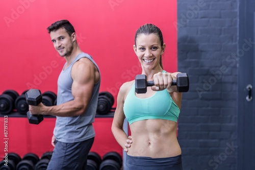 Smiling muscular couple lifting dumbbells