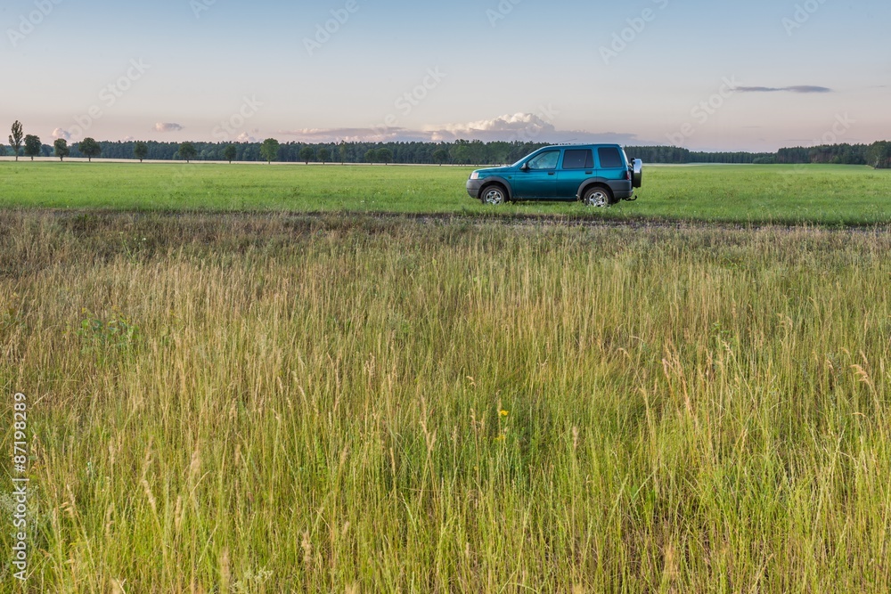 Fototapeta premium Rural grassland landscape with green off-road car