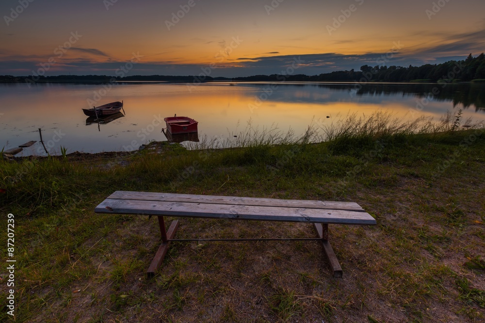 Beautiful lake sunset with bench on shore and fisherman boat
