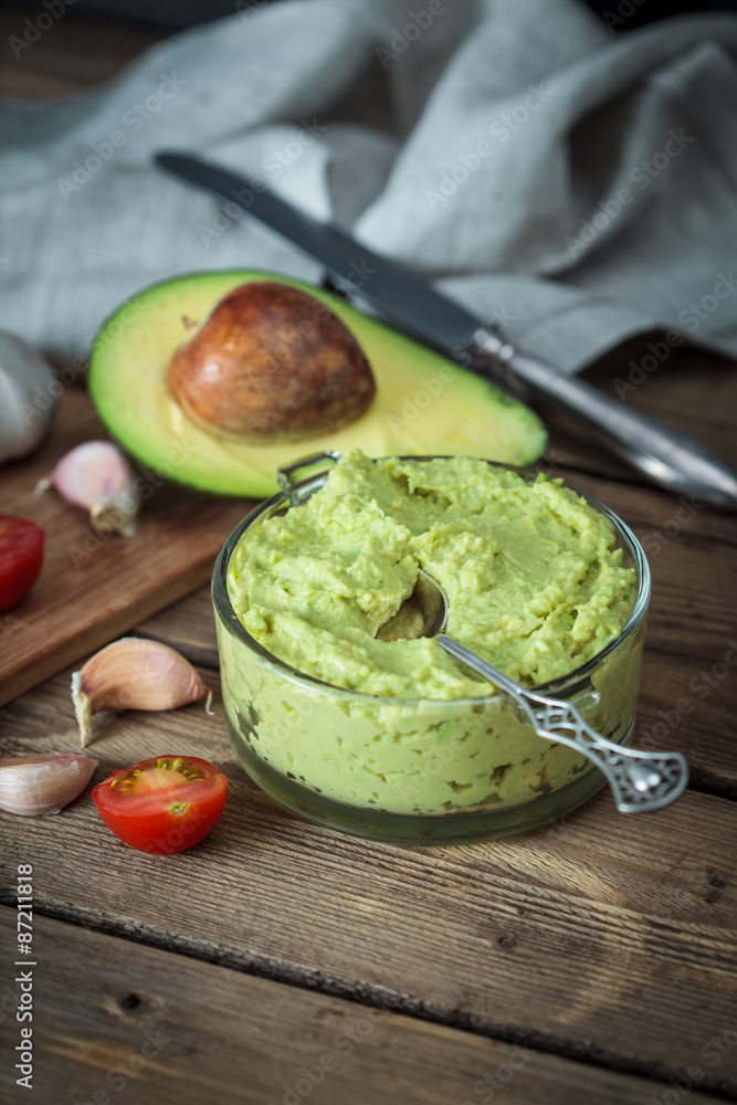 Guacamole on wooden table surrounded by its ingredients.. Guacamole on wooden table surrounded by its ingredients..