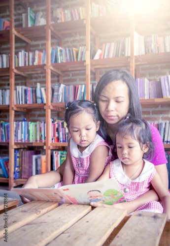 Mother and little daughter reading book together in library