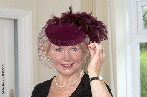 Elderly woman adjusting her maroon colored hat and veil with feathers photo