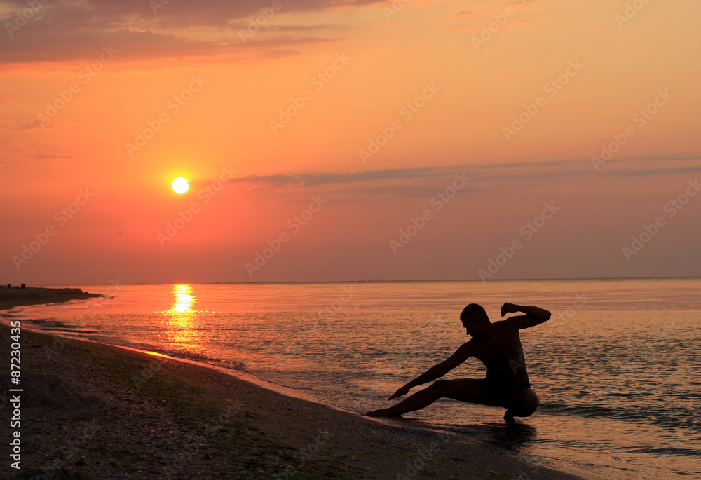 man silhouette doing wushu poses on the beach at sunrise