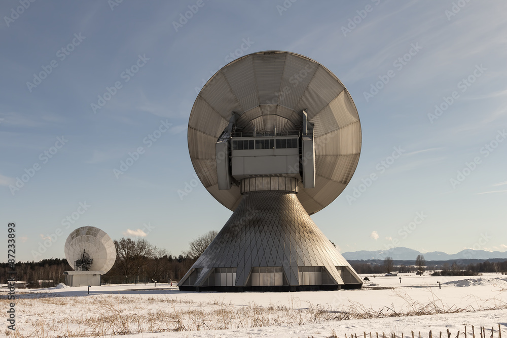 Two satellite dishes on a snow covered field with mountains in the background
