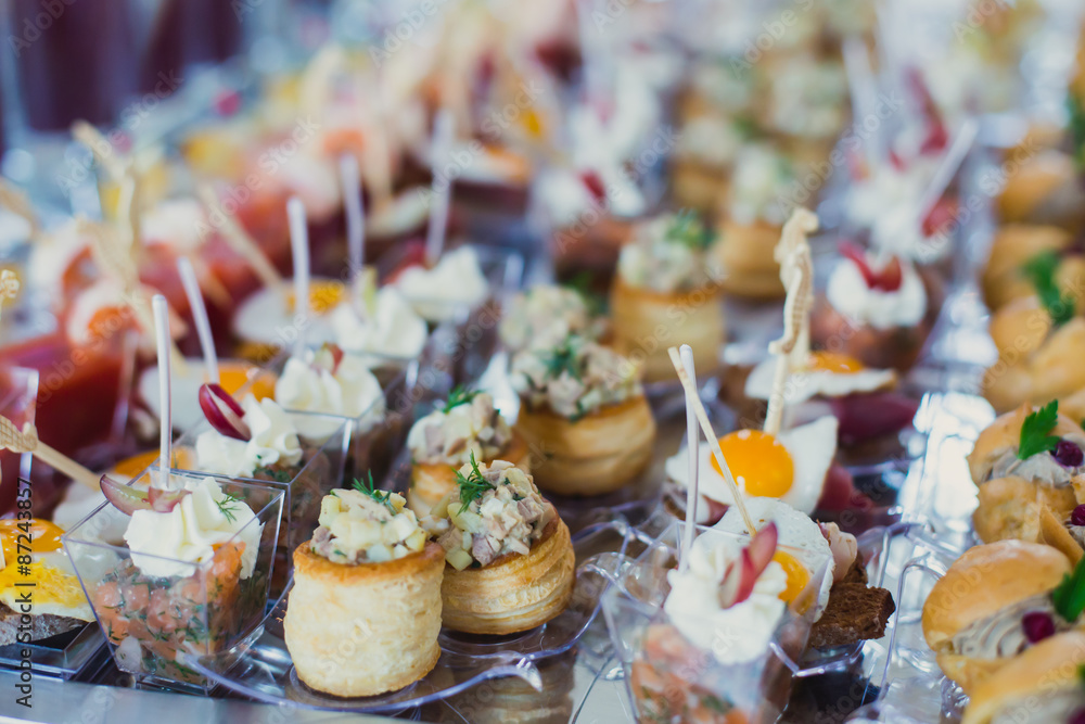 Beautifully decorated catering banquet table with different food snacks and appetizers with sandwich, caviar, fresh fruits on corporate birthday party event or wedding celebration 