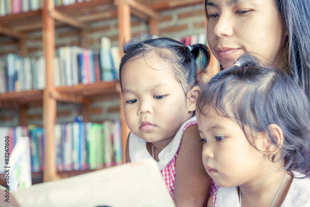 Mother and little daughter reading book together in library Mother and little daughter reading book together in library