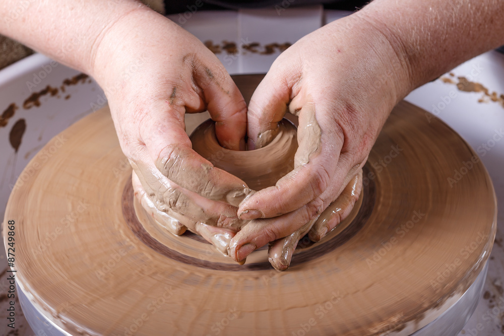 Hands working with clay on potter's wheel.