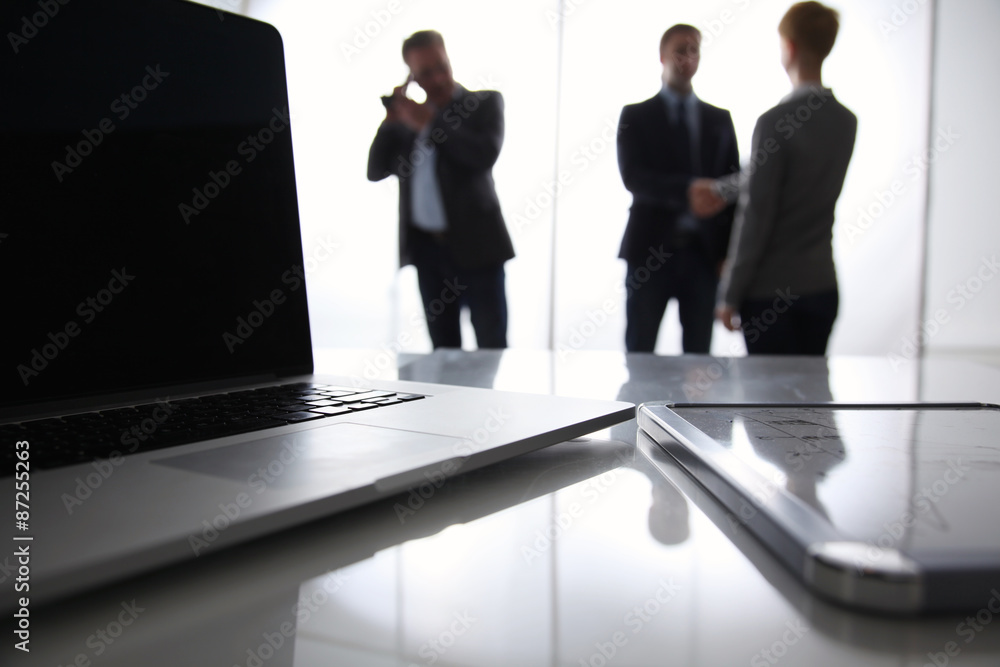 Fototapeta premium Laptop computer on desk , three businesspeople standing in the