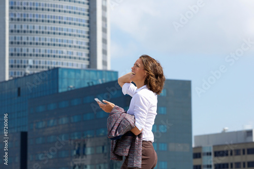 Smiling business woman walking in the city with cell phone