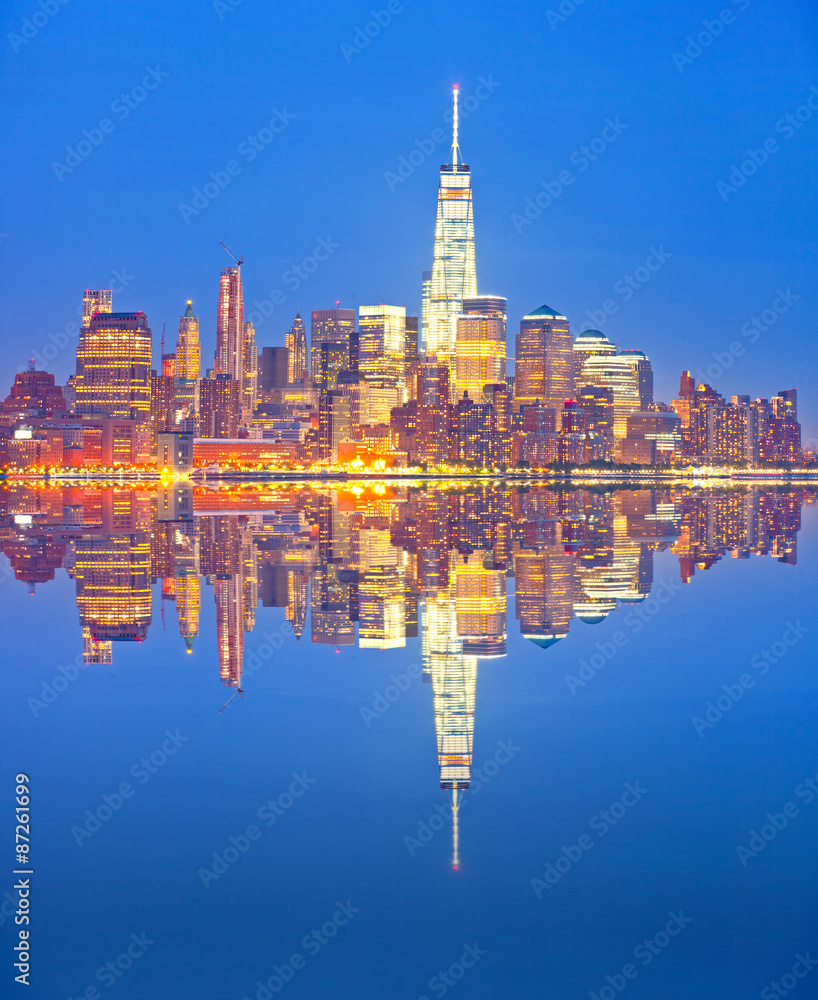 New York City skyline, financial district colorful illuminated buildings with reflections in downtown Manhattan at sunset