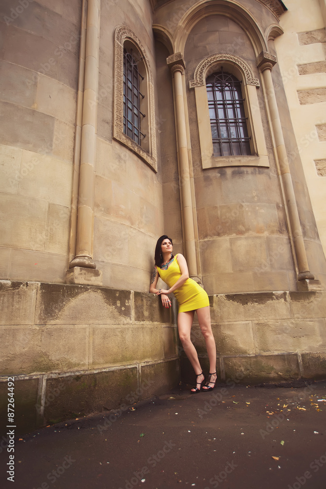 beautiful girl in a yellow dress leaned on old architectural bui