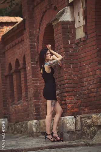 beautiful girl in a black dress stands near architectural struct photo