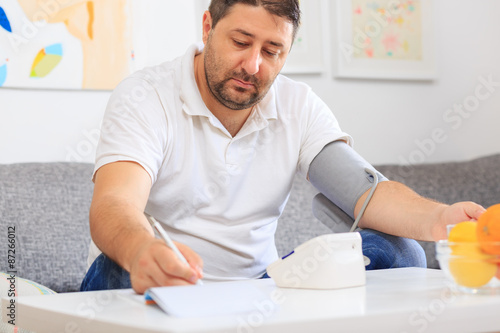 Man measuring his blood pressure and writing the results into his medical health diary