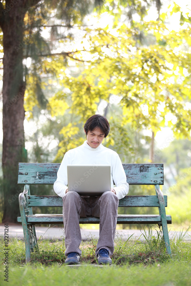 A young handsome man using laptop sitting on a bench in a park. A young handsome man using laptop sitting on a bench in a park.