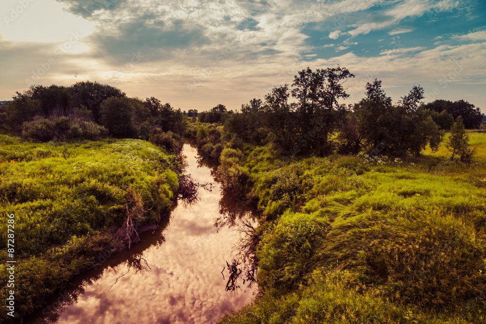 small river receding into distance on background of sunset clouds small river receding into distance on background of sunset clouds