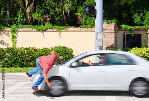 A man that is texting while driving runs over a pedestrian while the Cross Now sign is clearly visible showing that the pedestrian had the right of way. photo