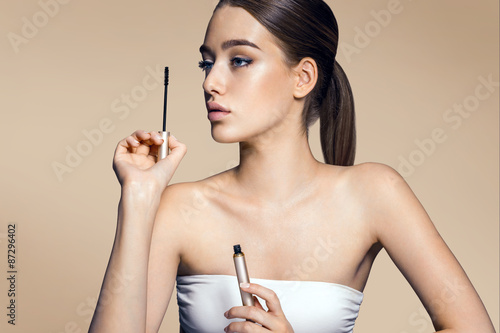 Bilde på lerret Charming young girl applying mascara / photos of appealing brunette girl on beig