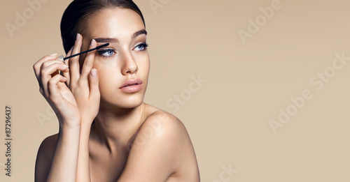 Mascara applying. Makeup closeup. Eyes make-up / photos of appealing brunette girl on beige background