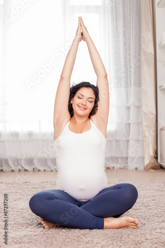 Attractive young pregnant woman is meditating on floor