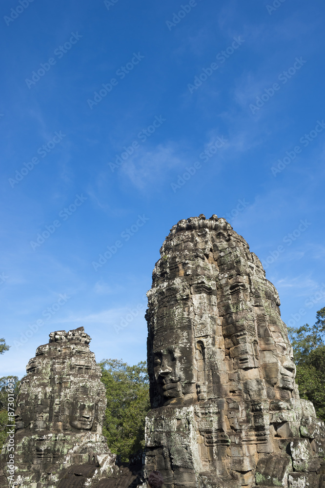 Angkor Thom Temple of Bayon stone face sculptures with green trees under bright blue sky 