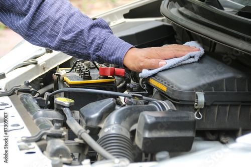 Man is cleaning his car engine with a rag.