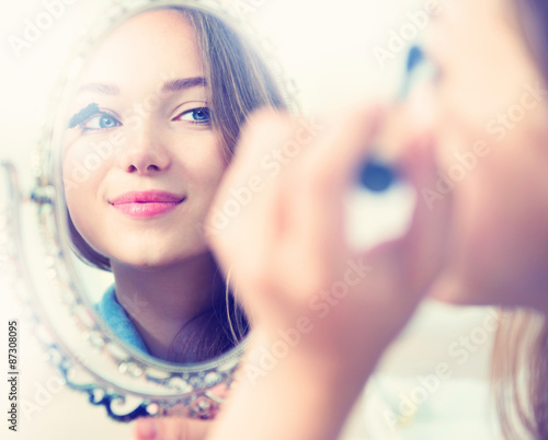 Beauty model girl looking in the mirror and applying mascara