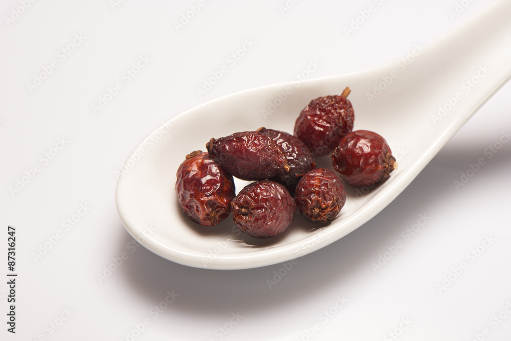 Dry berry rose hips in white ceramic spoon Dry berry rose hips in white ceramic spoon