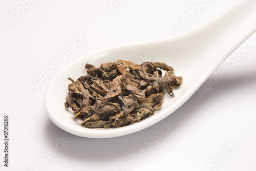 Heap of dry green tea leaves in white ceramic spoon