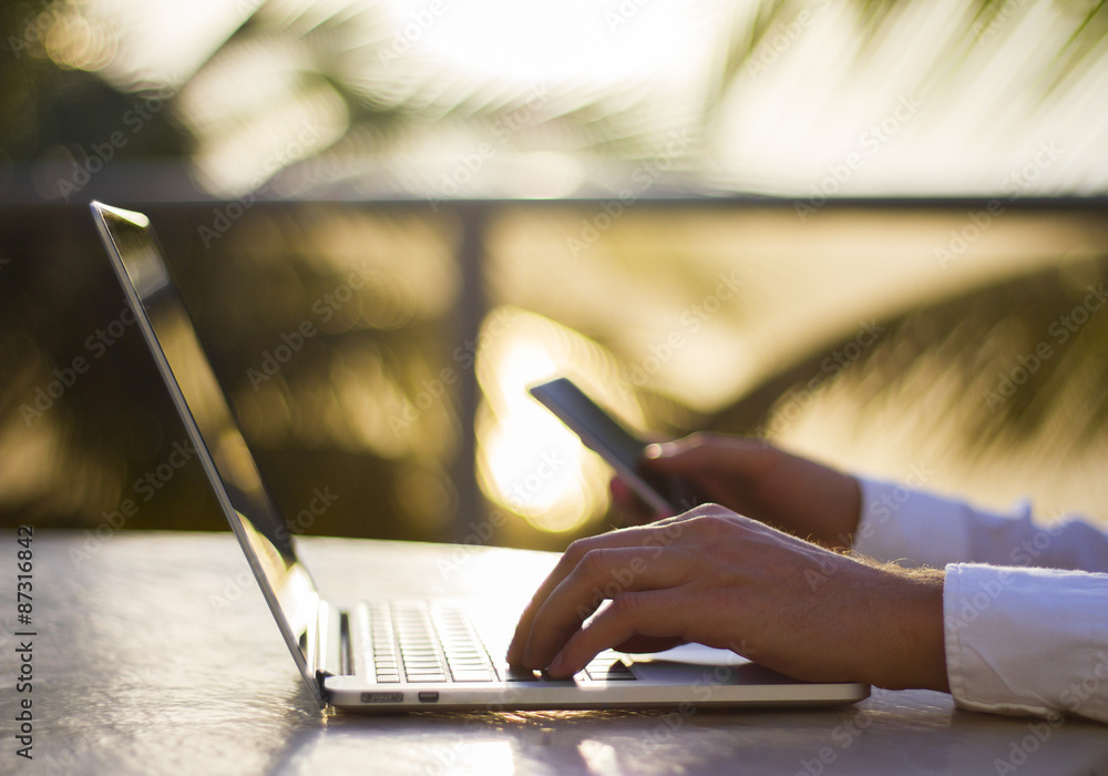 Naklejka premium a man working with a laptop and cell phone at sunset