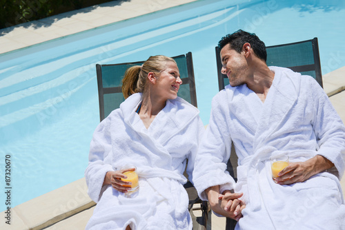 beautiful young couple resting in deck chairs with bathrobe by the pool of a thalasso resort