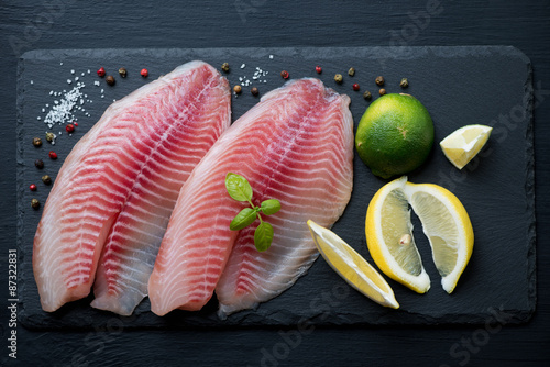 Stone slate plate with raw tilapia filets, view from above