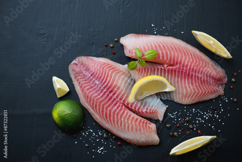 Raw tilapia filets with spices, lemon and lime, above view