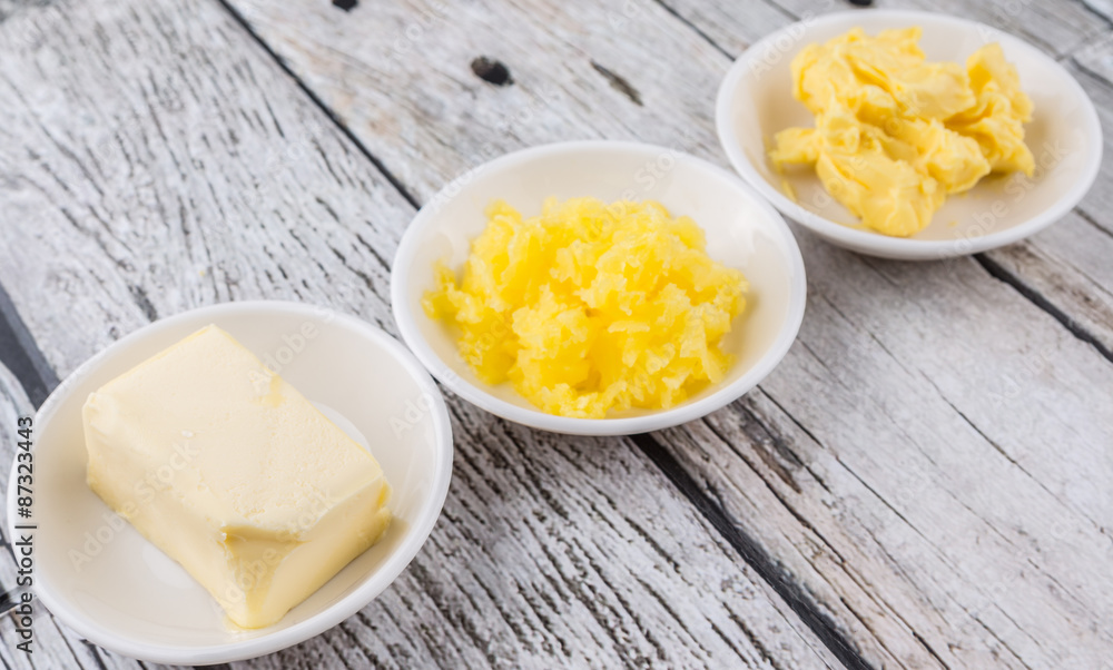 A block of butter, margarine and ghee in white bowls over rustic wooden background A block of butter, margarine and ghee in white bowls over rustic wooden background