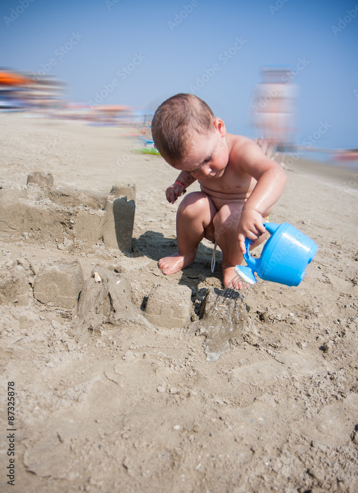 Little boy playing with sand and watering can at sea italy beach Little boy playing with sand and watering can at sea italy beach