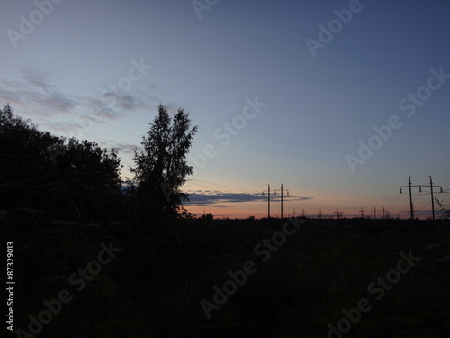 Силуэты линии электропередачи со столбами и проводами на фоне неяркого розоватого заката и синего неба