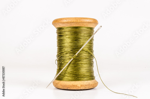 Vintage wooden green thread spool with needle isolated on white