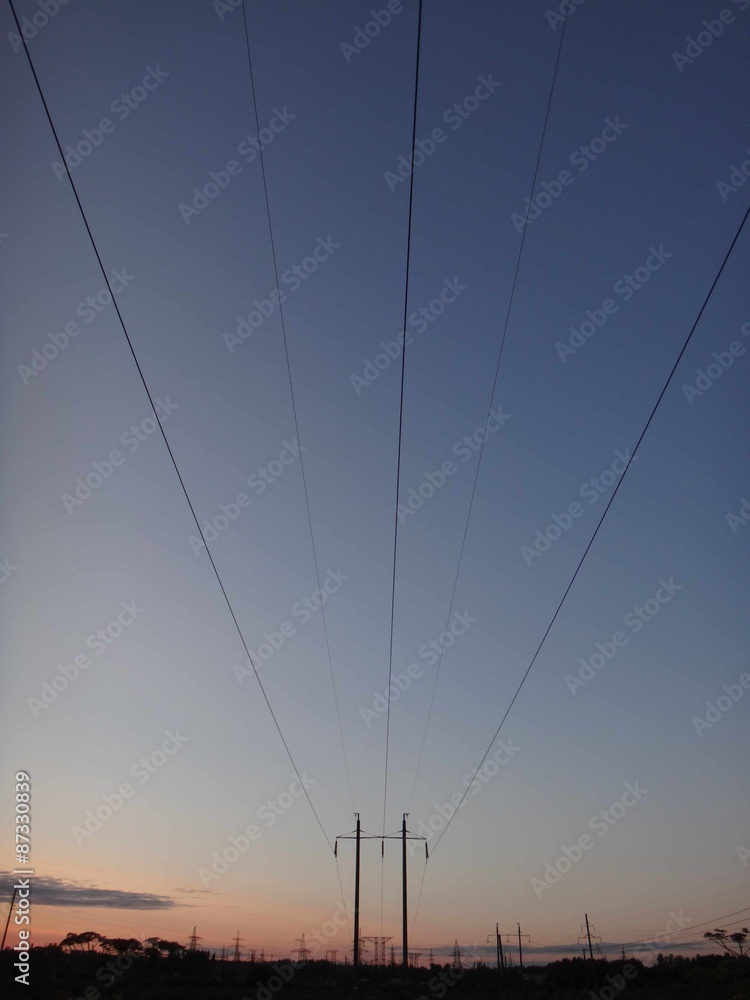 Силуэты линии электропередачи со столбами и проводами на фоне неяркого розоватого заката и синего неба