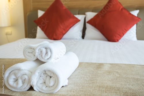 Close up of nice towels on white bed sheet with red pillow