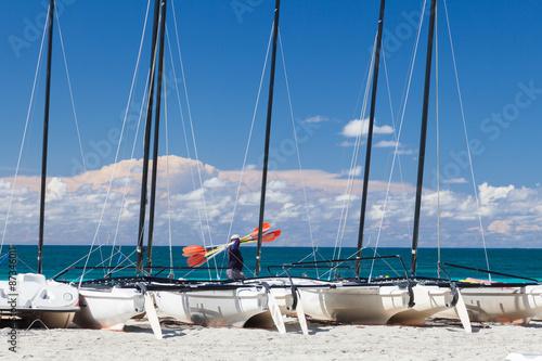 Man with oars goes on sea front. A lot of catamarans stay on the © ppklov