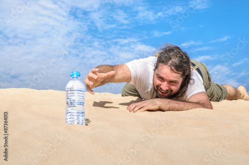 Thirsty man in the desert reaches for a bottle of water photo
