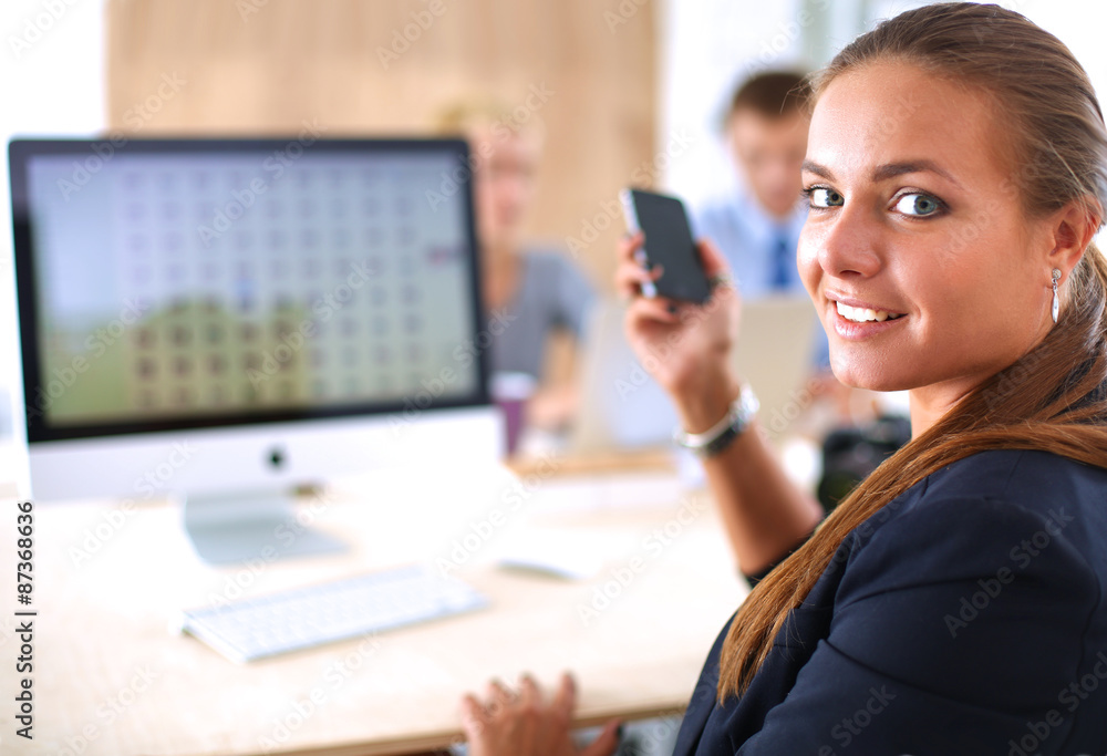 Young woman working in office, sitting at desk, using phone Young woman working in office, sitting at desk, using phone