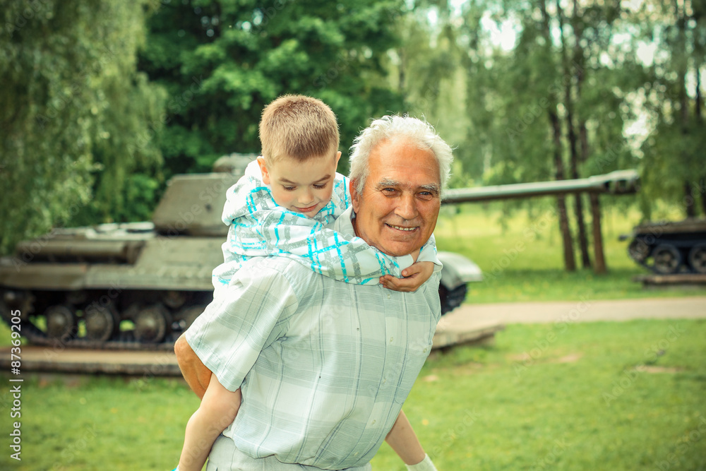 Grandfather and grandson are photographed on a background of vintage tank Grandfather and grandson are photographed on a background of vintage tank