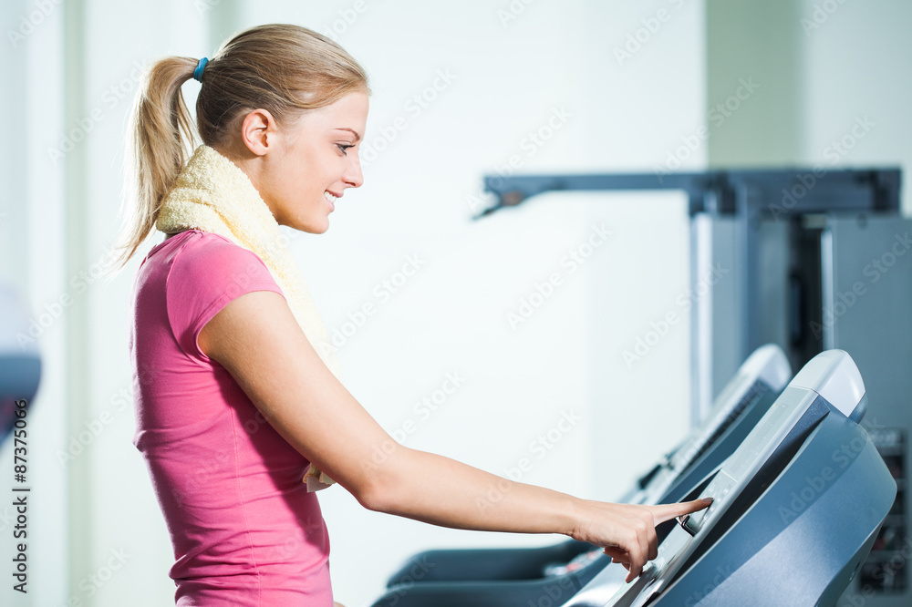 Happy woman adjusts treadmill in gym Happy woman adjusts treadmill in gym