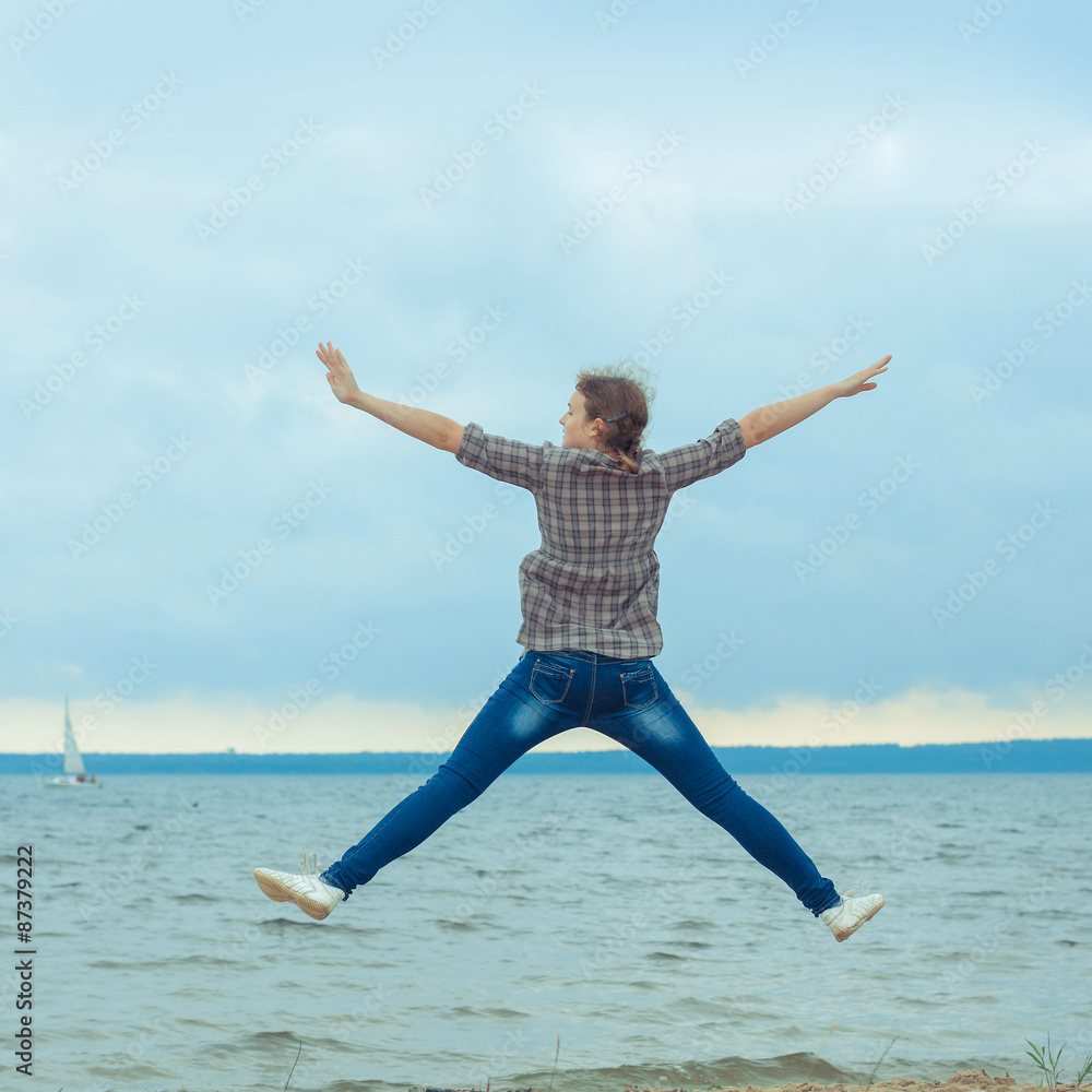 cheerful teen girl jumping on the beach in cloudy windy weather cheerful teen girl jumping on the beach in cloudy windy weather