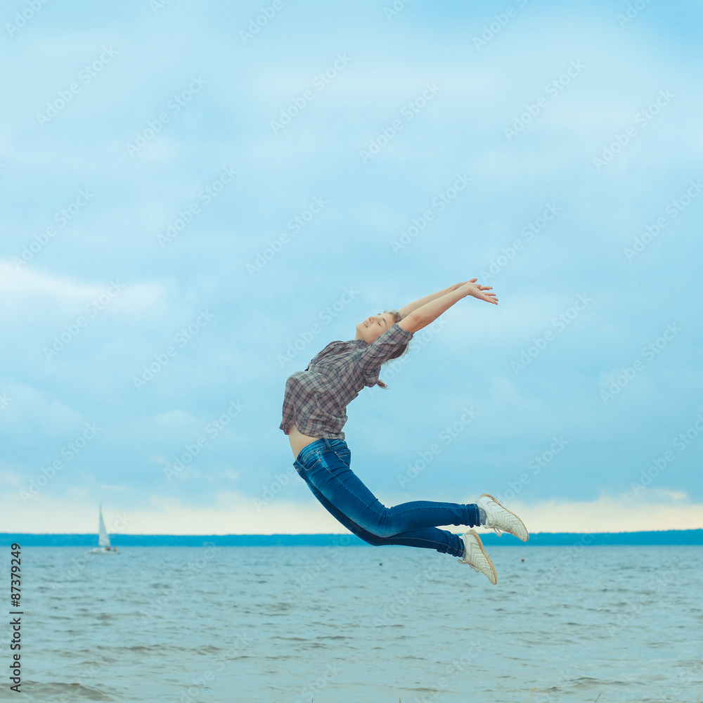 cheerful teen girl jumping on the beach in cloudy windy weather cheerful teen girl jumping on the beach in cloudy windy weather
