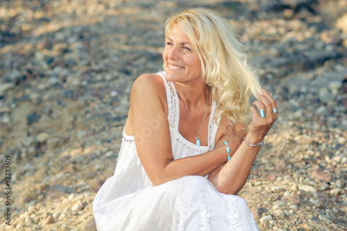 romantic portrait of a beautiful older woman. Mature beautiful blonde in a white dress walks on the  road